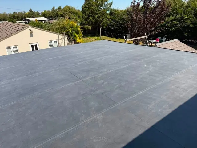 Completed black EPDM rubber flat roof, wide view with houses behind